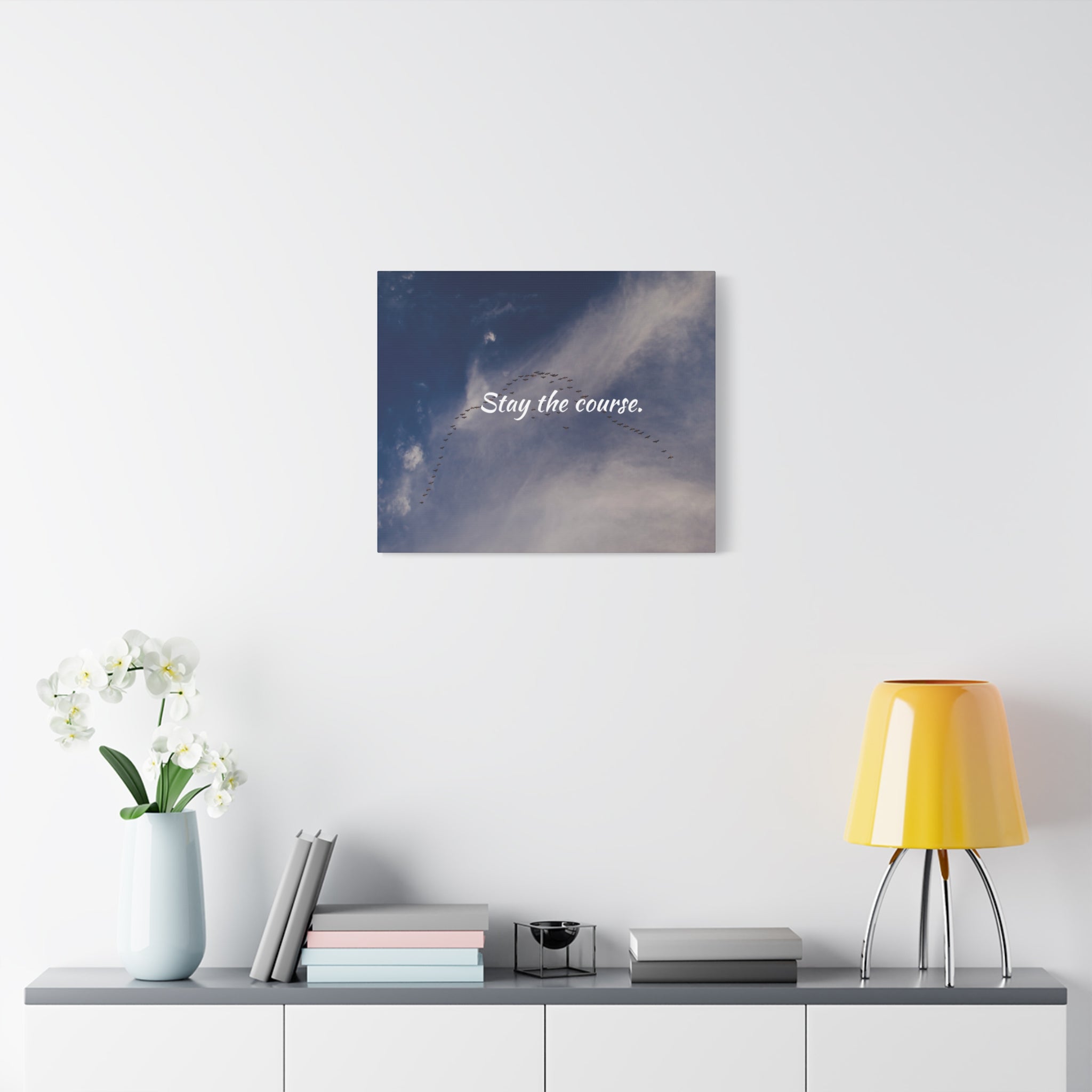 Canvas print with 'Stay the course.' text on a wall above a shelf with decor items.