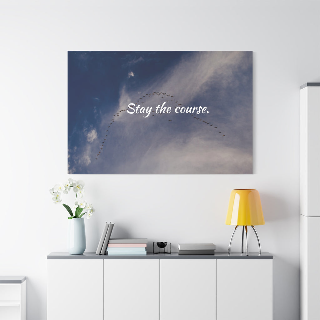 Wall art with 'Stay the course.' text above a desk with decor items.