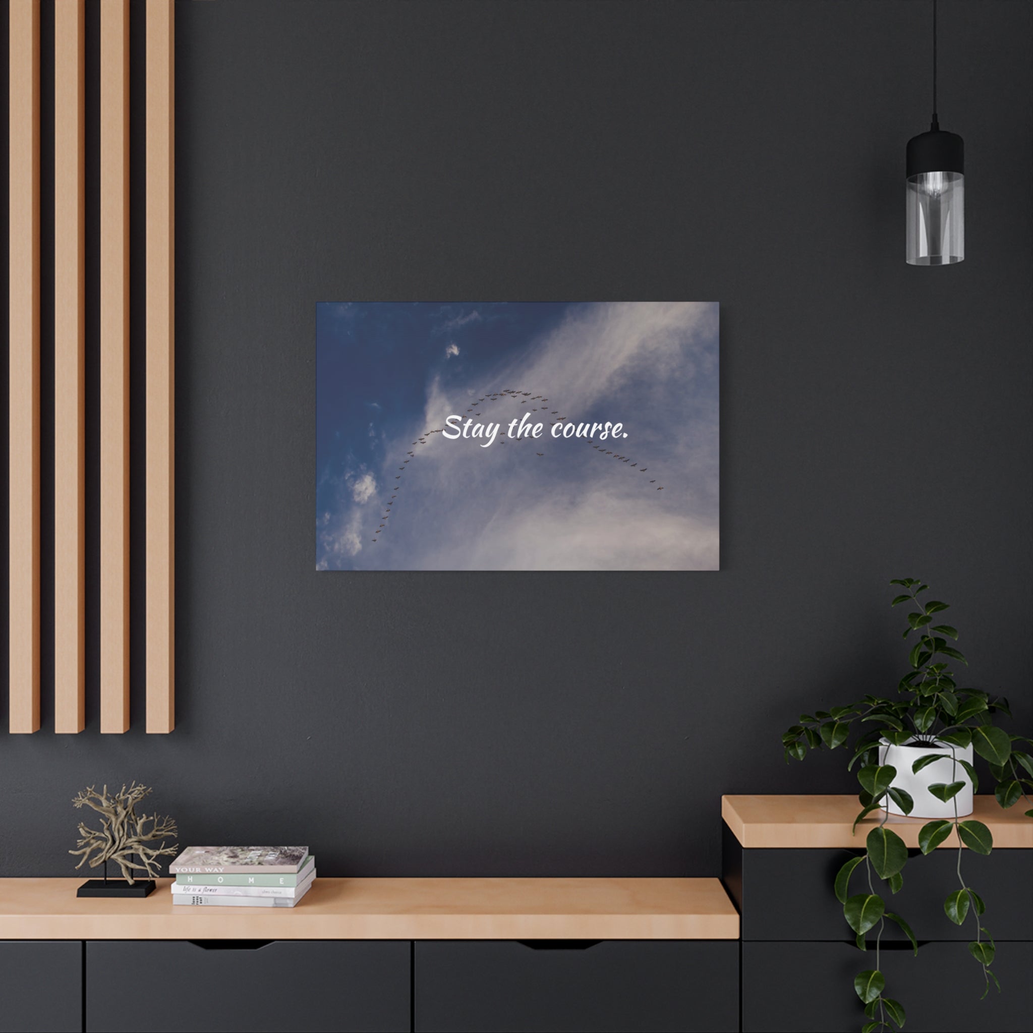 Art print with 'Stay the course.' text on a dark wall above a wooden shelf.