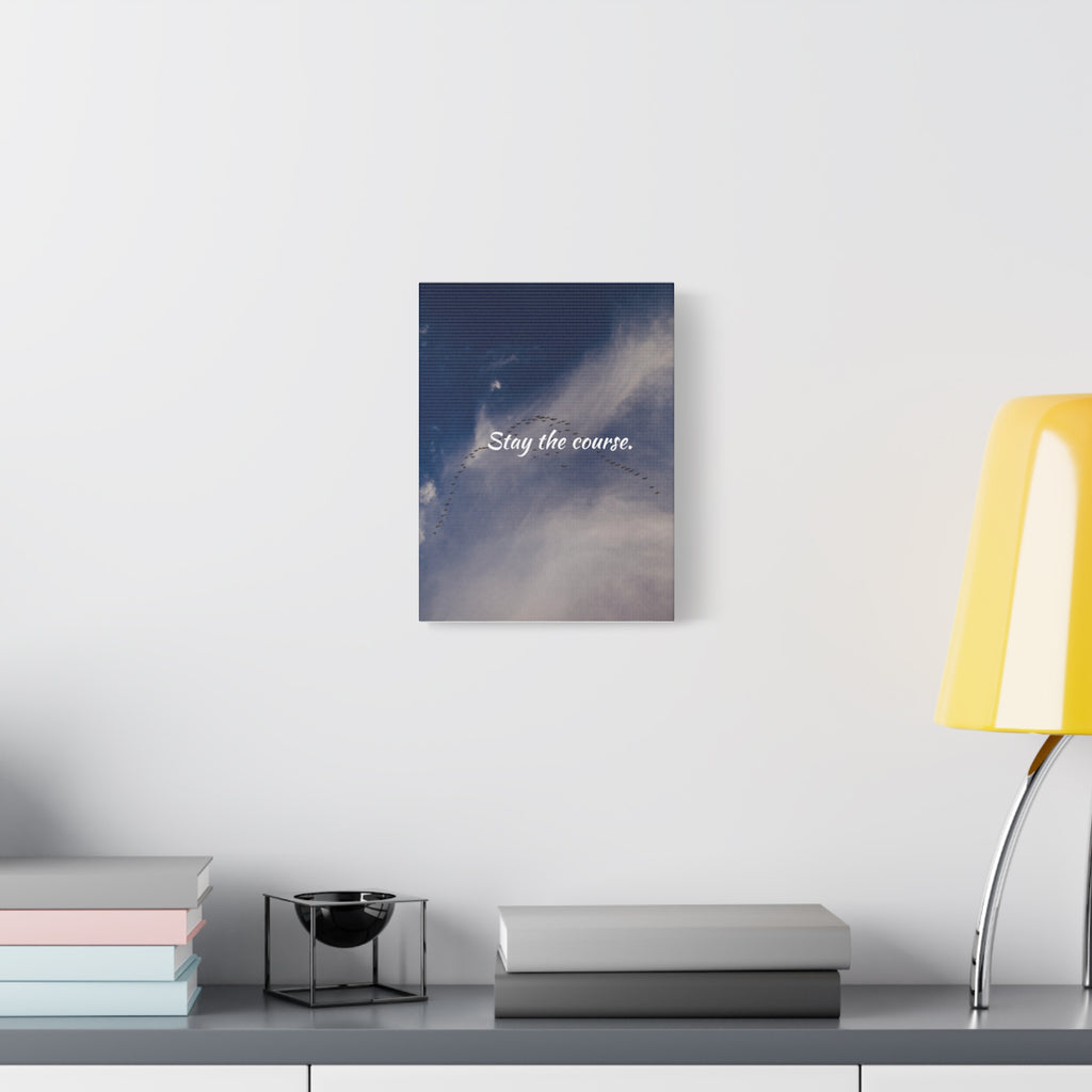 Canvas print with 'Stay the course.' text on a wall above a desk with books and a lamp.