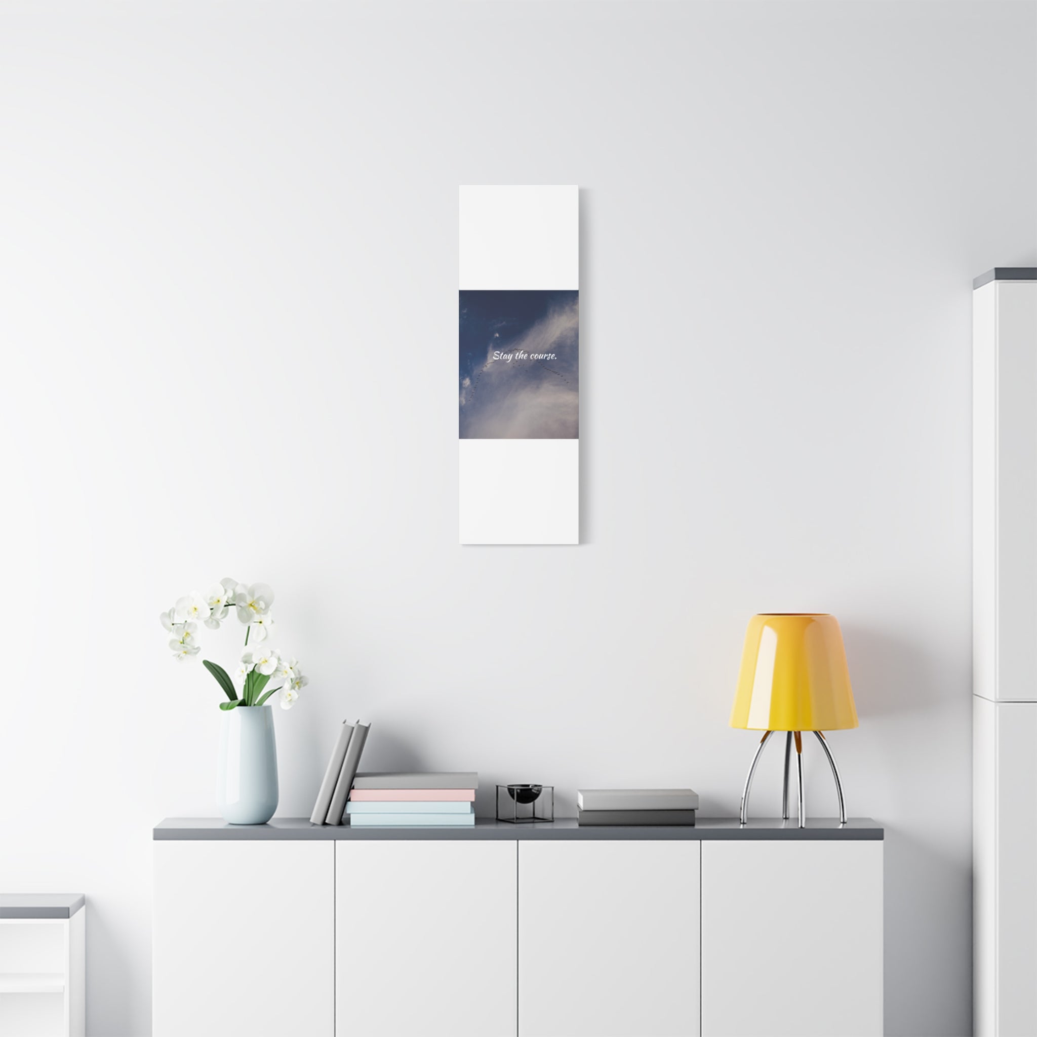 Modern interior with a yellow lamp, white vase with flowers, and framed picture on a white wall.