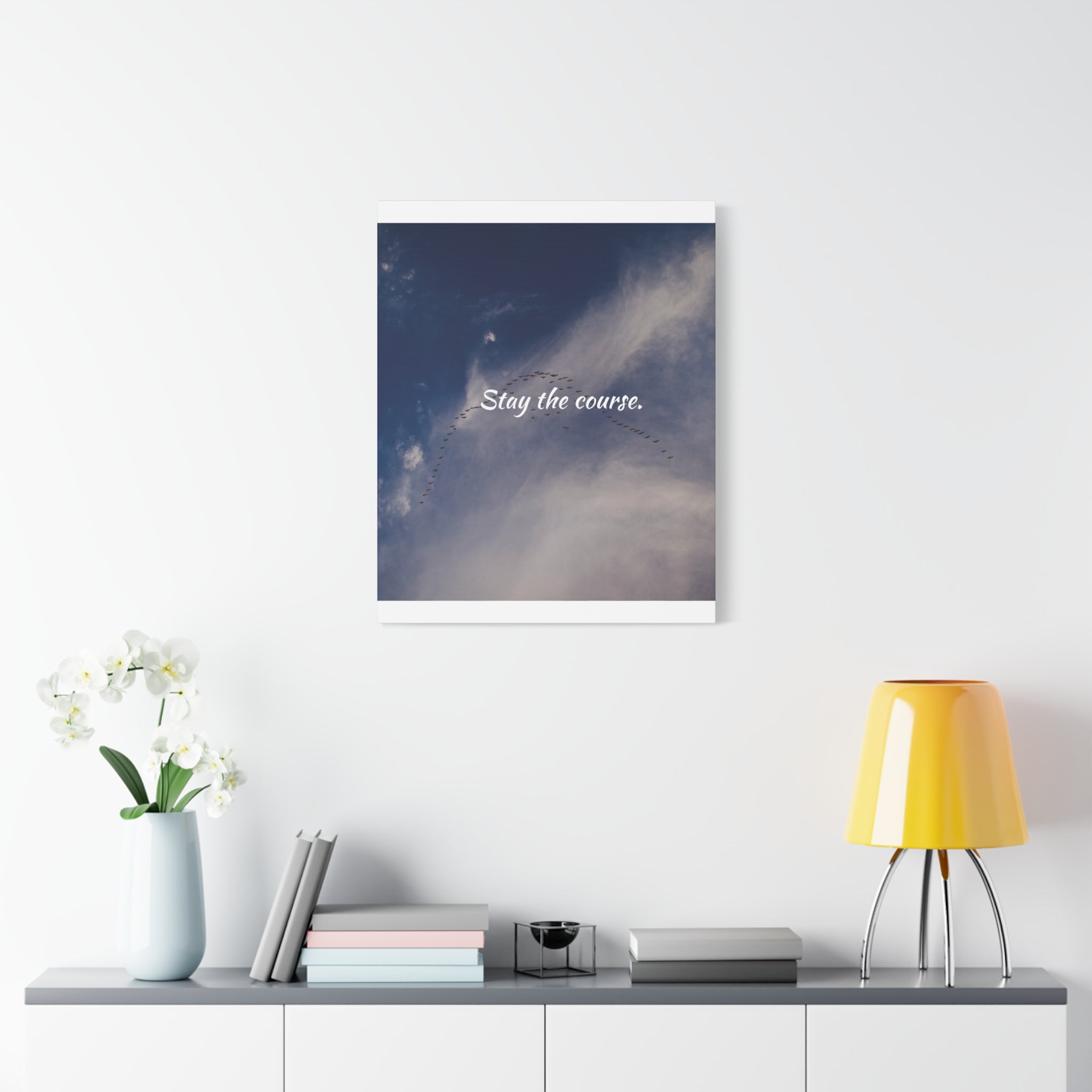 Framed artwork with 'Stay the course' text above a shelf with decor items on a white wall.