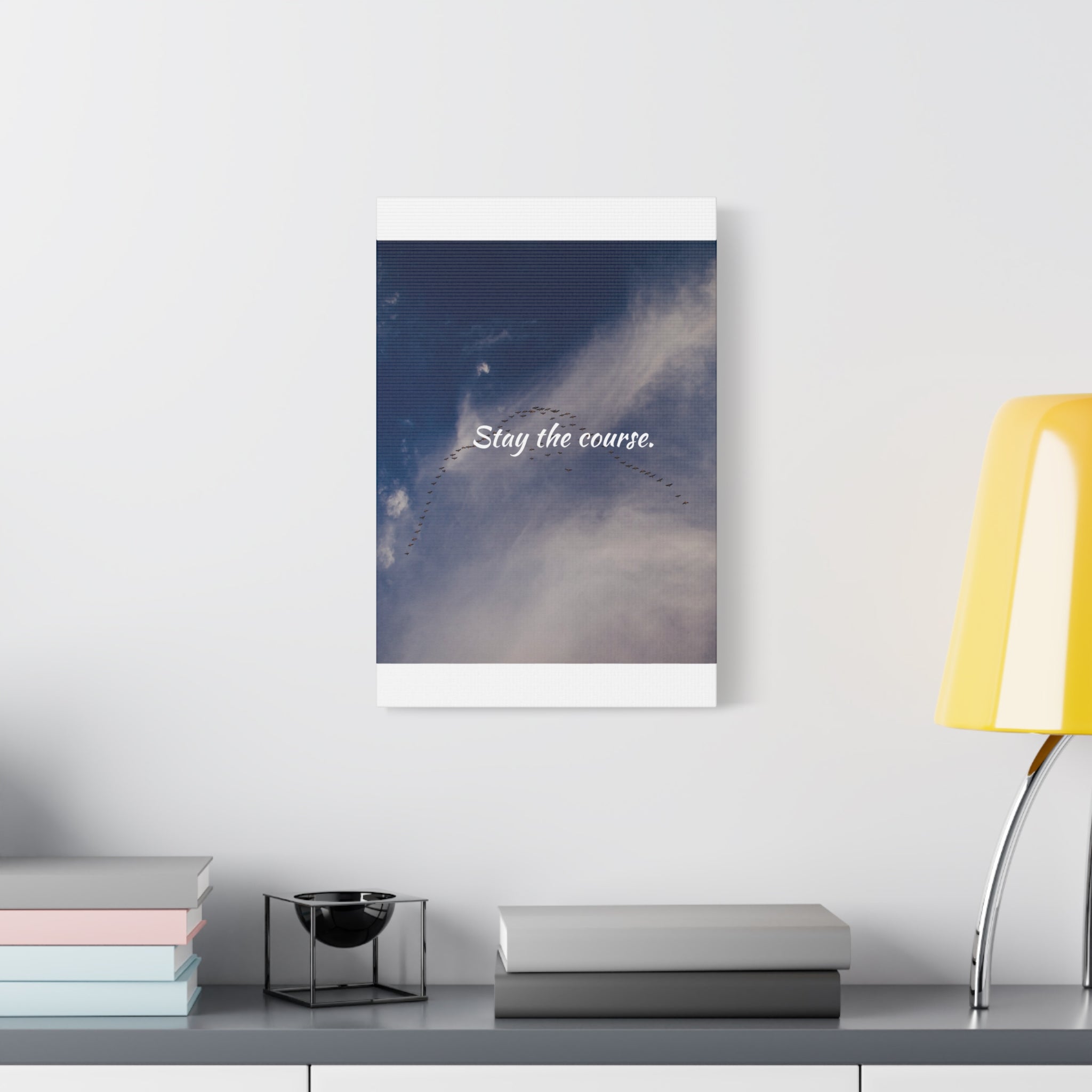 Framed artwork with 'Stay the course.' text on a shelf with books and a lamp.