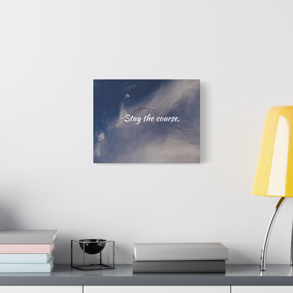 Wall art with 'Stay the course.' text on a blue and white abstract background, placed on a shelf with books and a lamp.