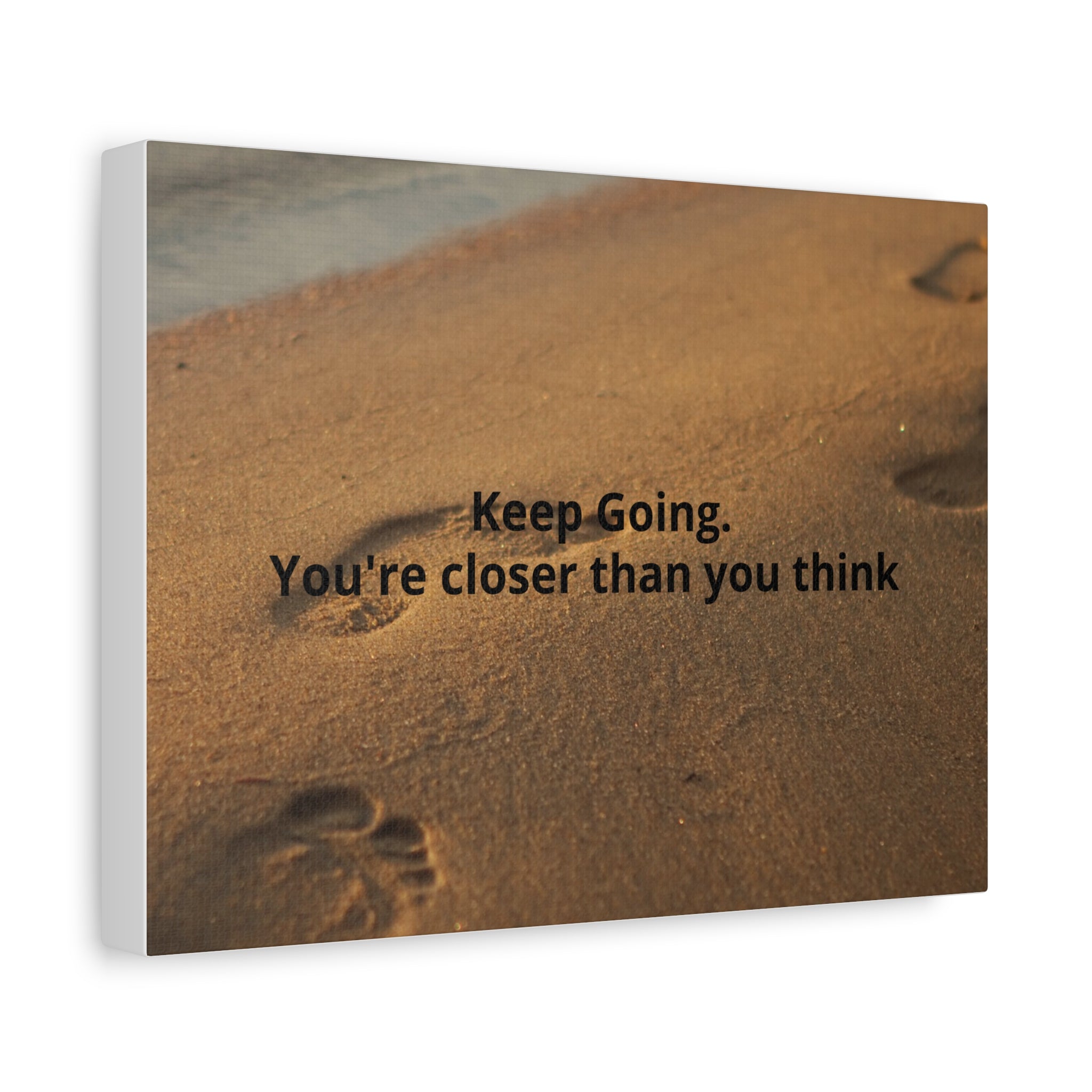 Motivational quote 'Keep Going. You're closer than you think' on sand with footprints.
