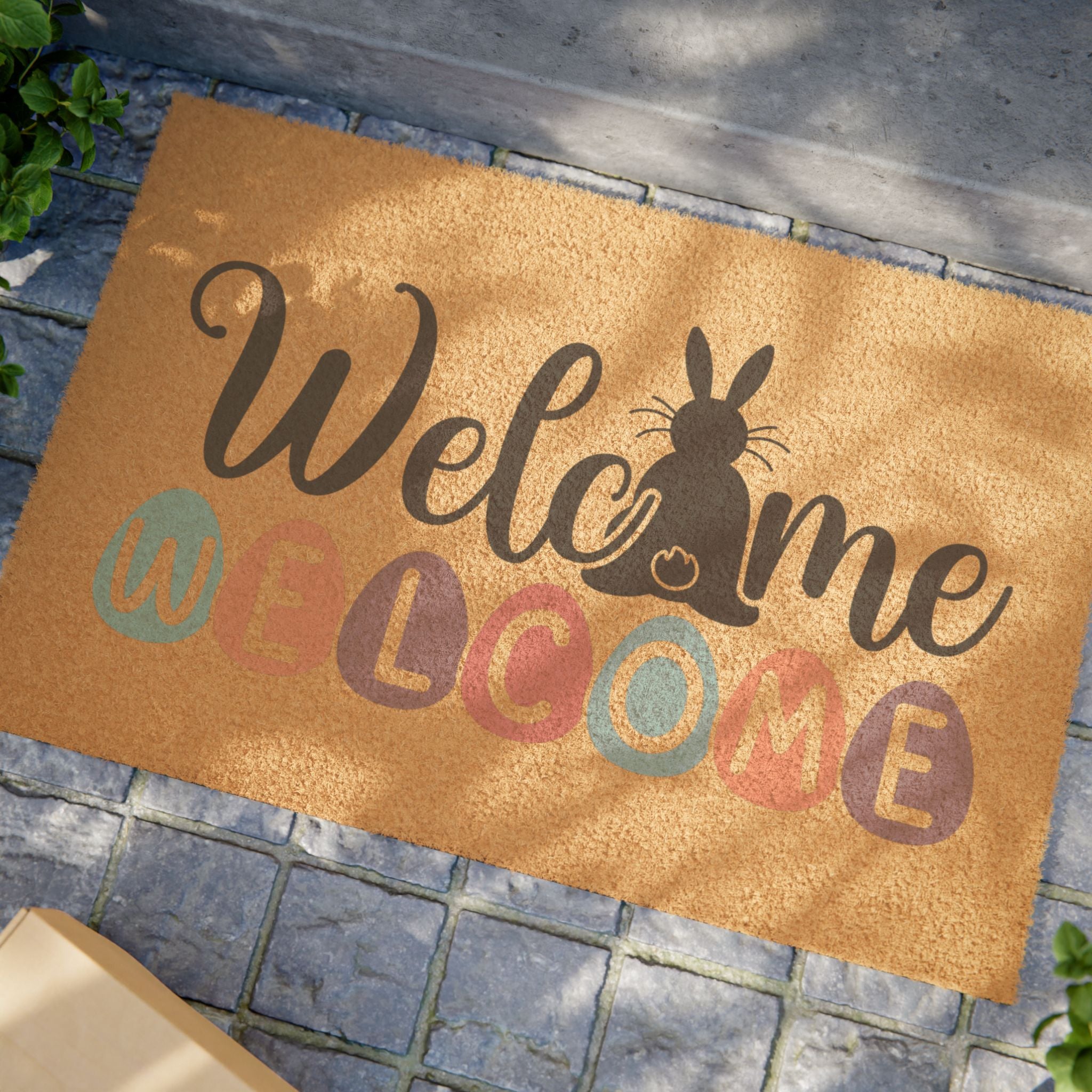 Doormat with 'Welcome' text and rabbit silhouette on a stone pavement.