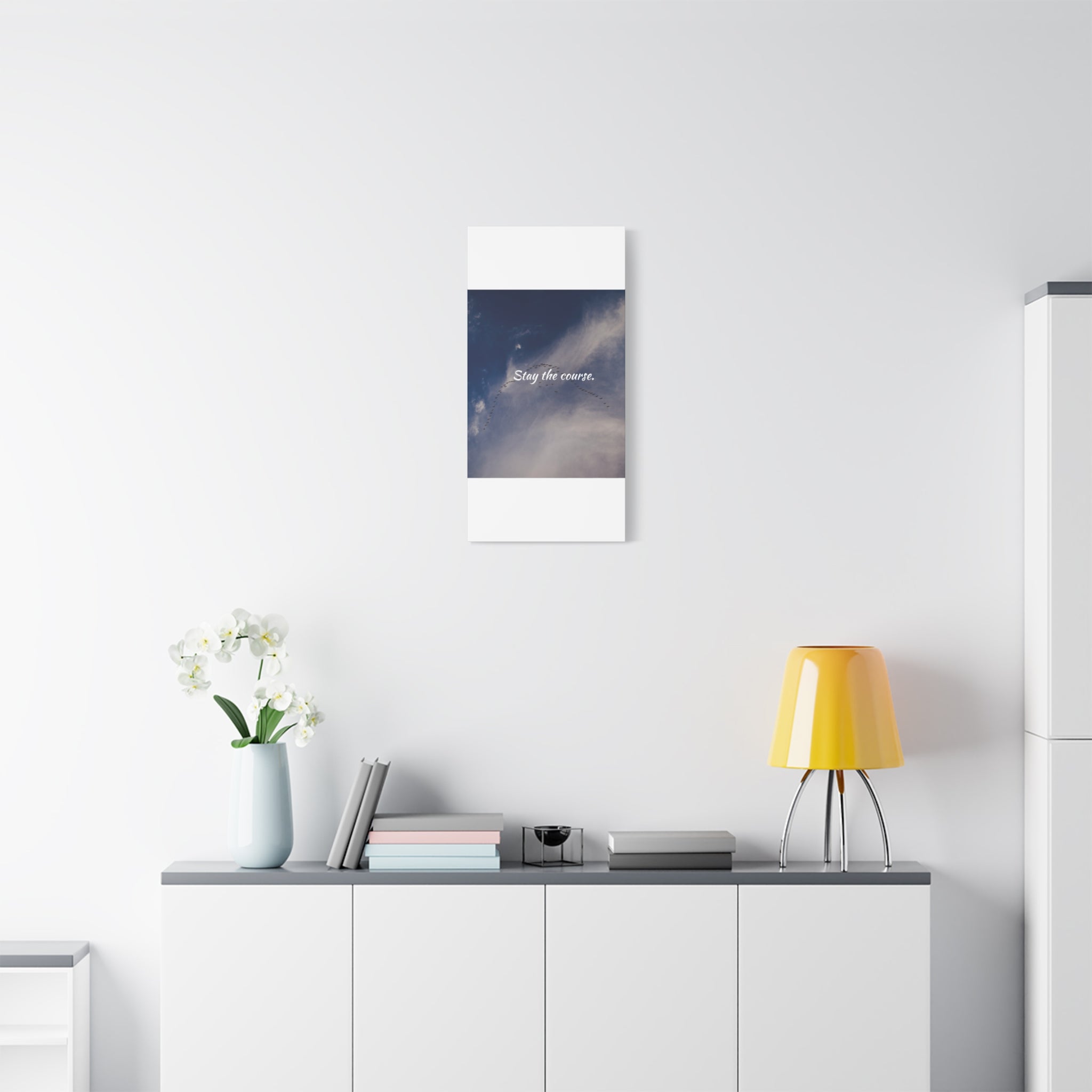 Modern interior with a yellow lamp, vase with flowers, and framed picture on a white wall.