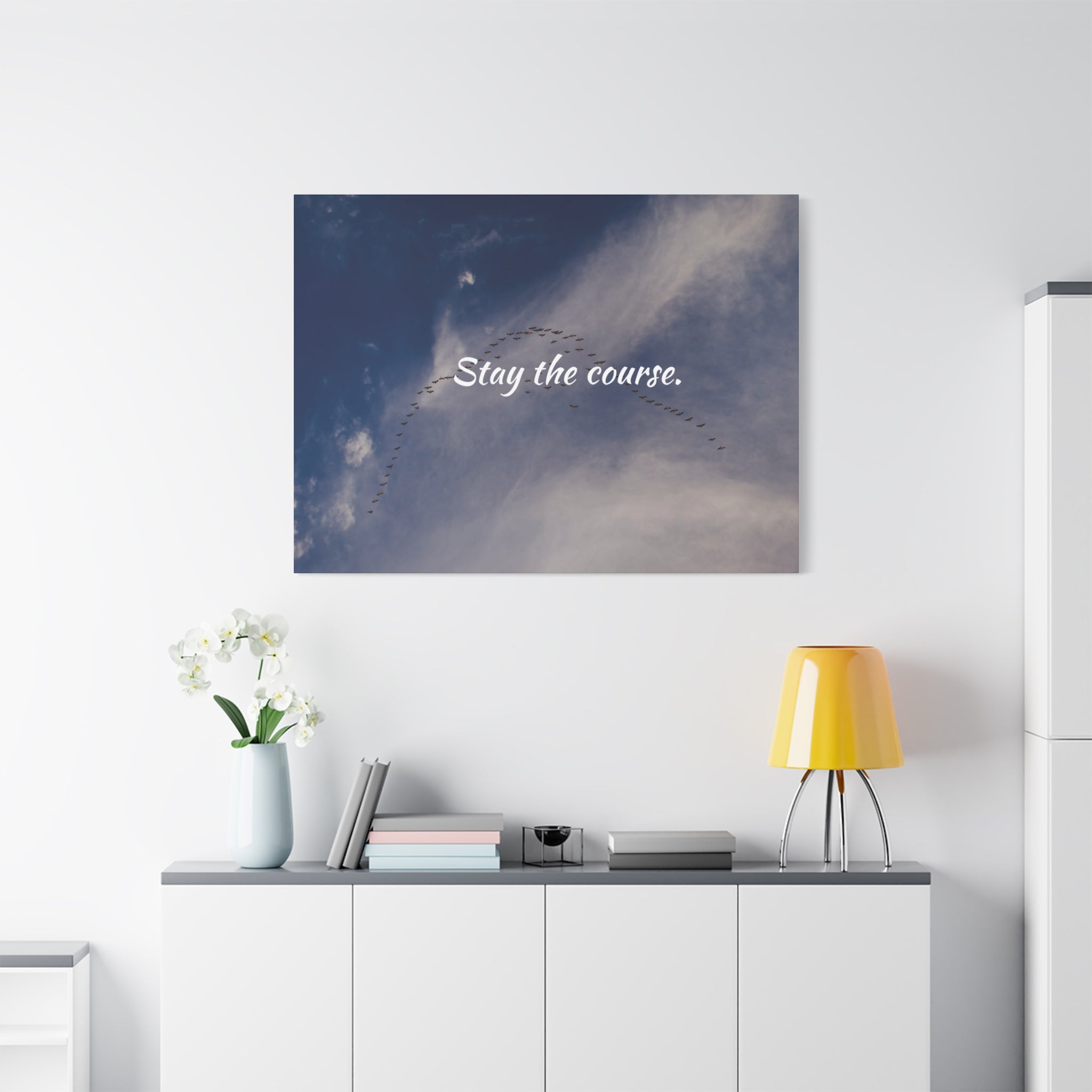 Wall art with 'Stay the course.' text above a white cabinet with decor items.