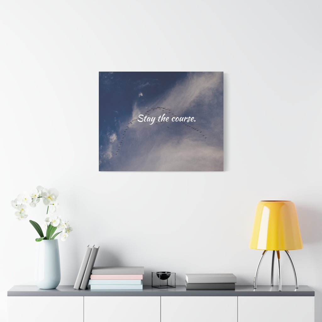 Wall art with 'Stay the course.' text on a blue sky background, displayed above a shelf with decor items.