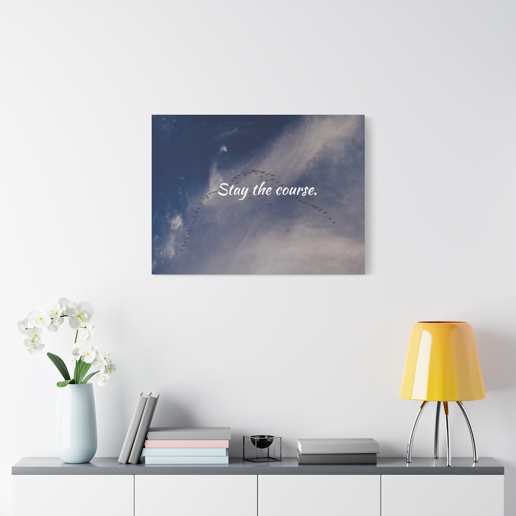 Wall art with 'Stay the course' text above a shelf with decor items on a white wall.