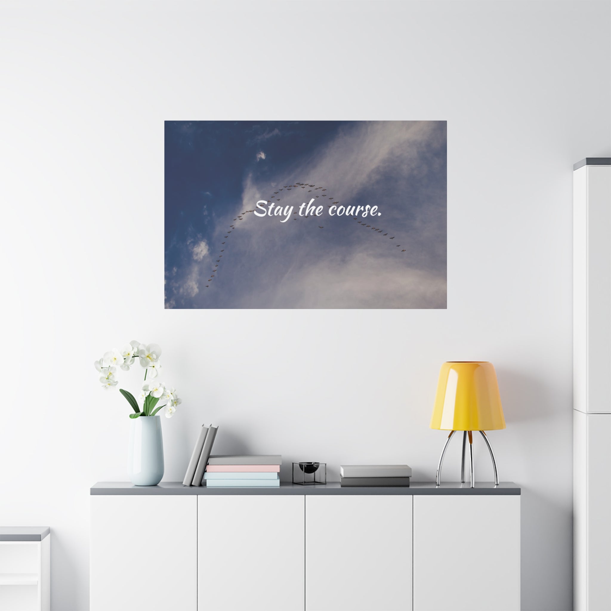Poster with 'Stay the course.' text on a wall above a white cabinet with decor items.