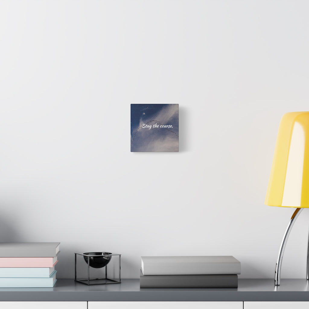 Canvas print with motivational quote on a wall above a desk with books and a lamp.