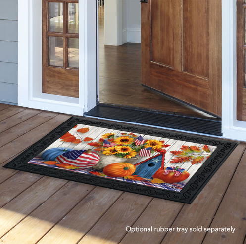 Decorative doormat with autumn design featuring pumpkins, sunflowers, and American flags on a wooden floor.