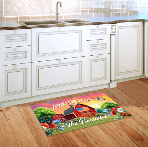 Decorative doormat with a barn design and 'America the Beautiful' text on a wooden floor in a kitchen.