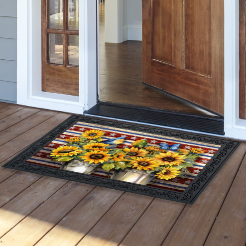 Decorative doormat with sunflower design on a wooden floor outside a house.