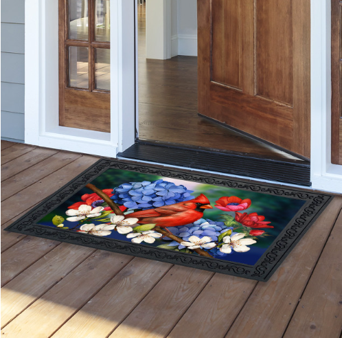 Decorative doormat with floral design on a wooden floor outside a house.