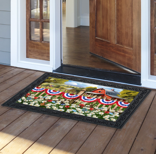 Decorative doormat with patriotic design on a wooden floor outside a house.