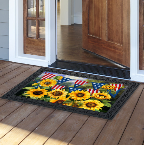 Decorative doormat with sunflowers and American flags on a wooden floor.
