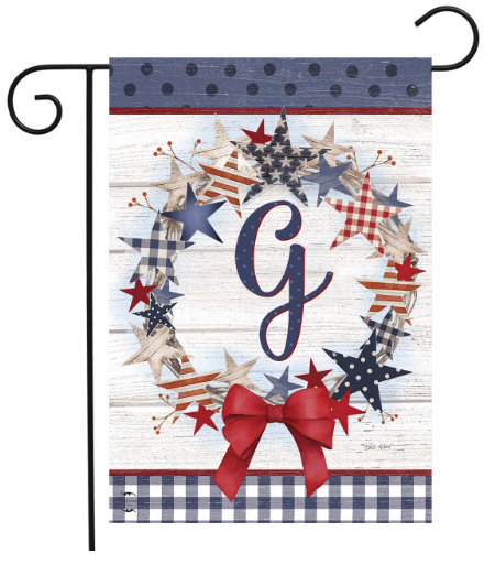 Decorative garden flag with stars, a bow, and the letter 'G' on a wooden background.