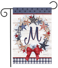 Decorative garden flag with stars, a bow, and the letter 'M' on a wooden background.