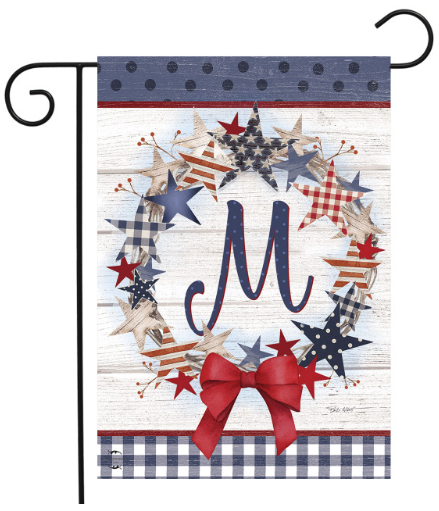 Decorative garden flag with stars, a bow, and the letter 'M' on a wooden background.