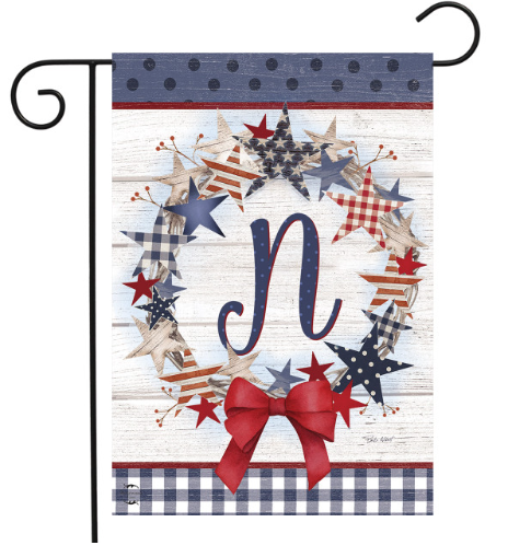 Decorative garden flag with stars, a bow, and the letter 'N' on a wooden background.