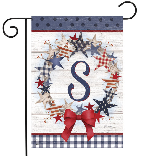 Decorative garden flag with stars, a bow, and the letter 'S' on a wooden background.
