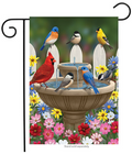 Decorative garden flag with birds around a fountain and colorful flowers.