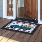 Decorative doormat with a blue truck design on a wooden floor outside a house.