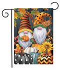 A decorative garden flag hanging from a black metal scroll-style stand. The flag features a fall-themed illustration with two gnome figures, pumpkins, sunflowers, autumn leaves, and the words 'I Love Fall' against a dark wood-plank background.
