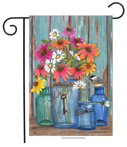 Decorative garden flag with colorful flowers and blue jars against a wooden background.