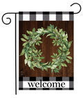 Decorative garden flag with a green wreath and 'welcome' text on a wooden background.
