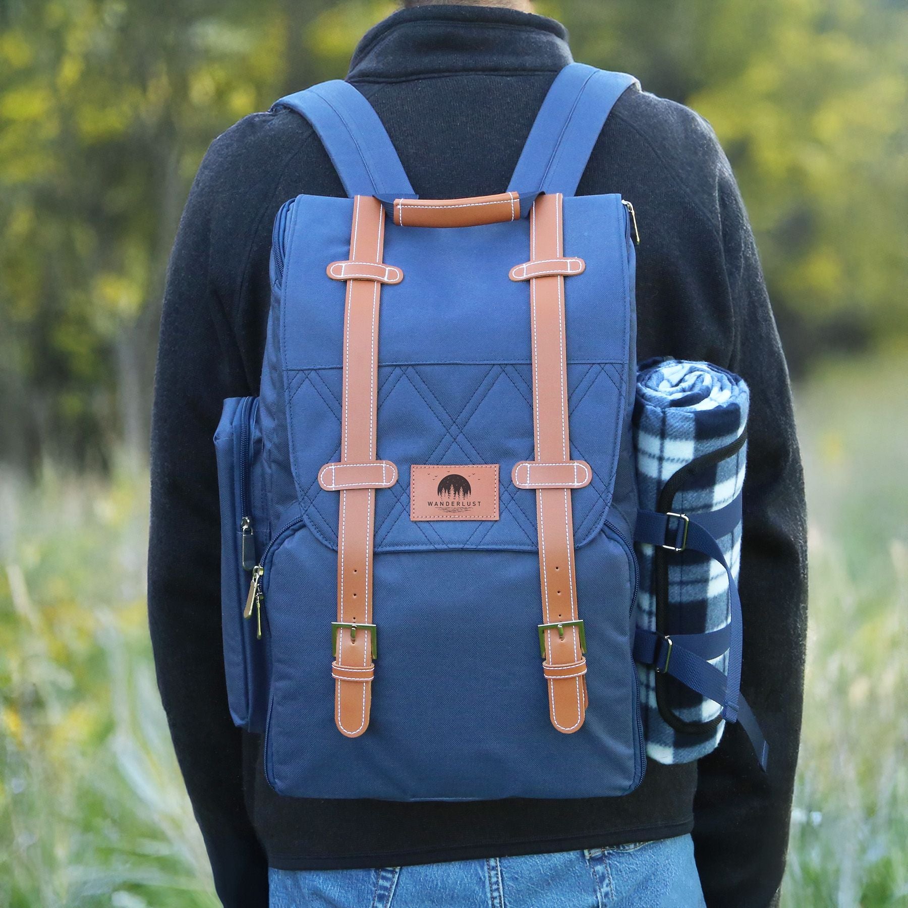 Person wearing a blue backpack with brown straps and a branded leather patch in a natural setting
