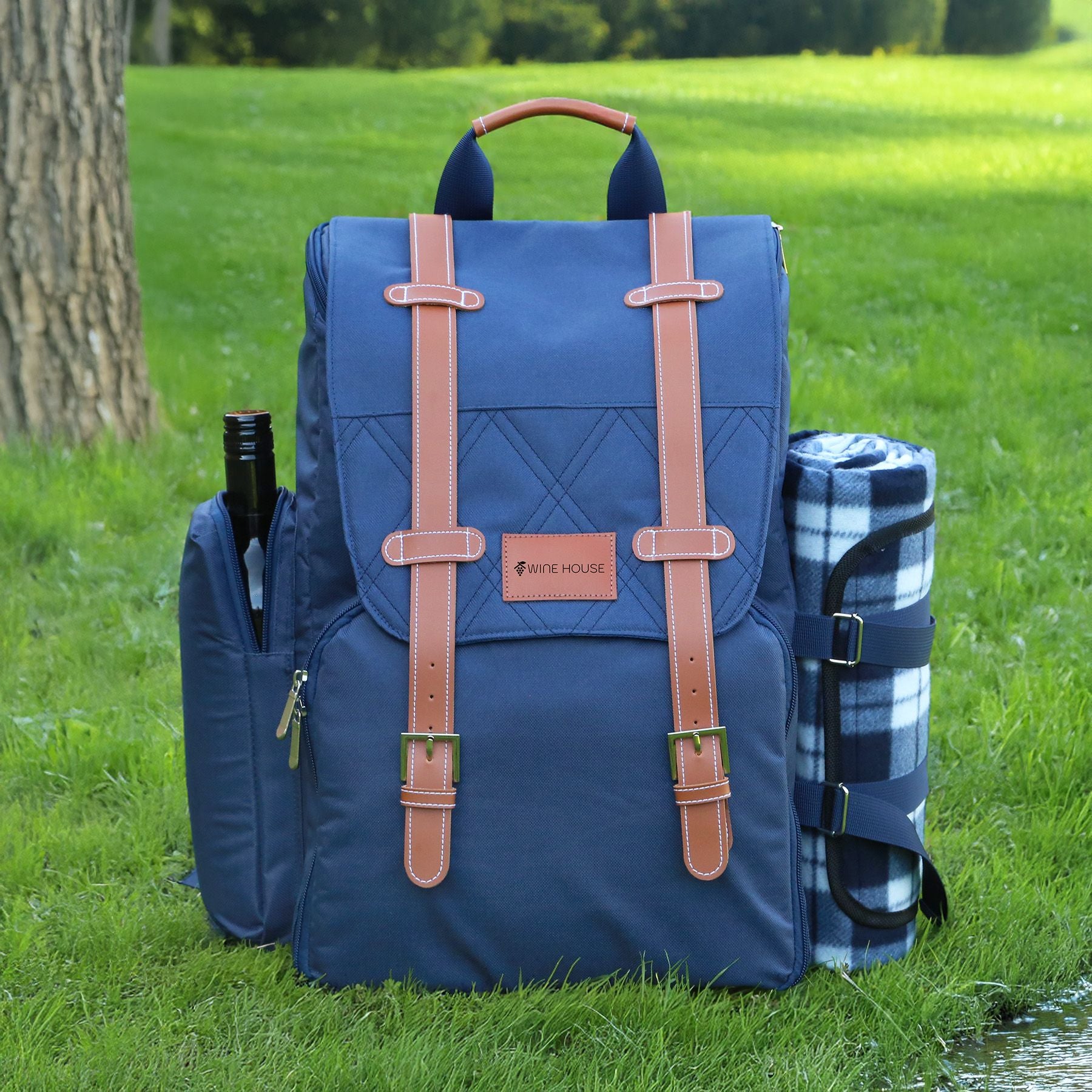 Blue backpack with brown straps on grass, accompanied by a picnic blanket and bottle.