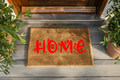 Doormat with 'HOME' in red letters on a wooden floor, flanked by plants.