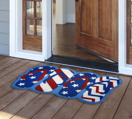 Decorative doormat with American flag design on a wooden floor outside a house.