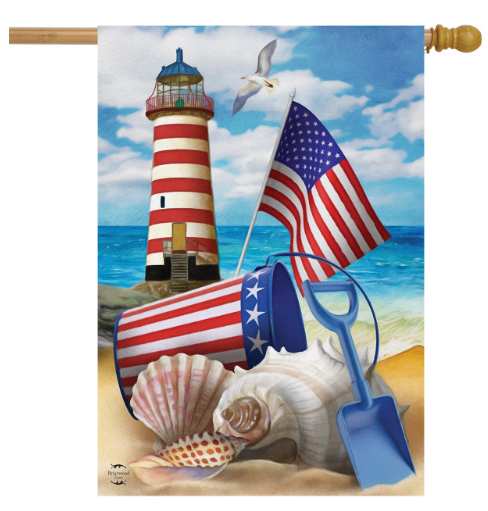 Decorative flag with a lighthouse, American flag, sand bucket, shovel, and shells on a beach.