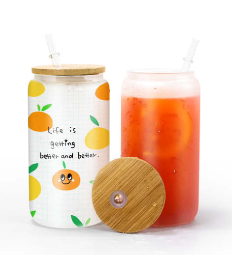 Glass Can with a wooden lid with Life Is Getting Better and Better text and lemon graphics and a glass of red juice on a white background