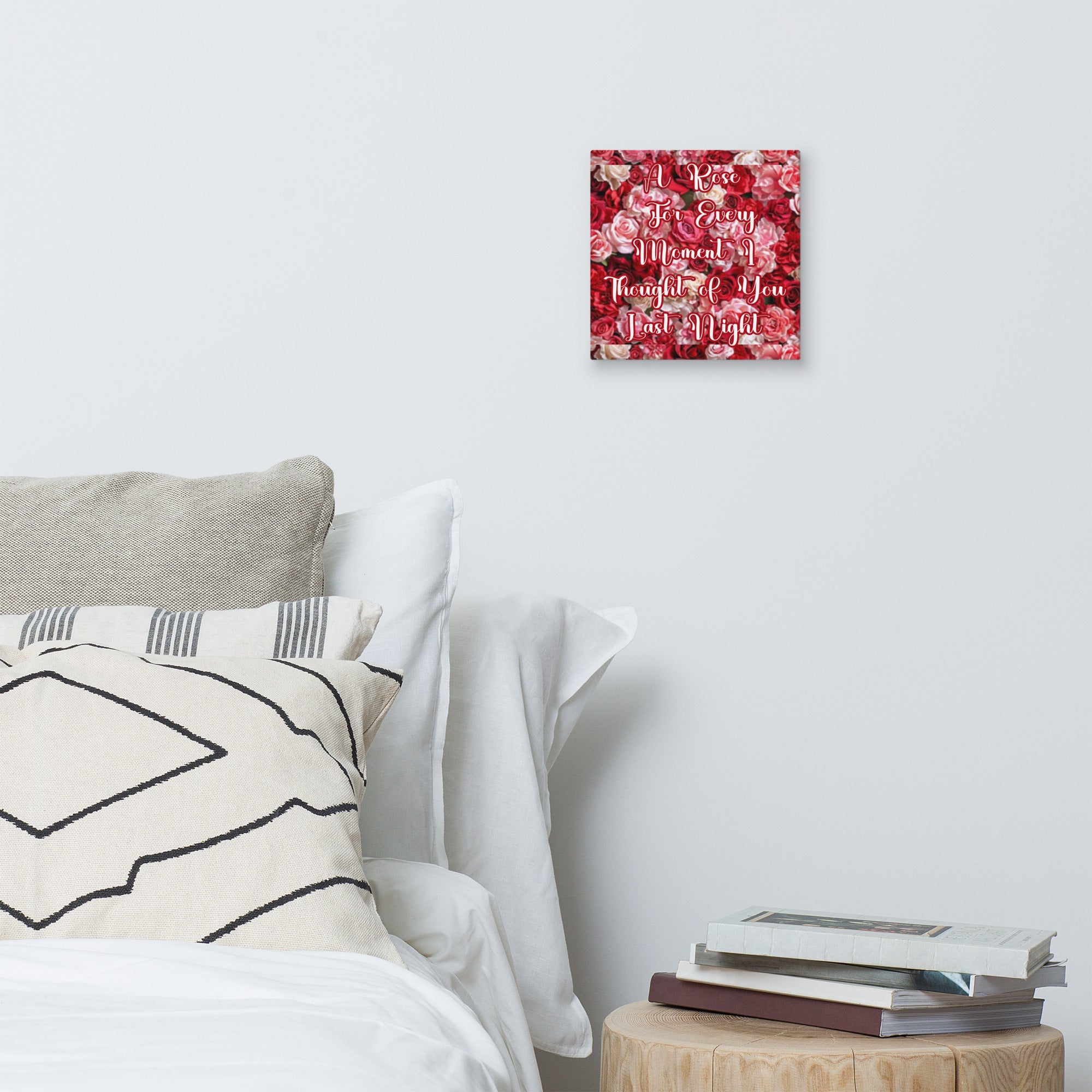 Decorative wall art with floral pattern and text above a bed with pillows and books on a nightstand.