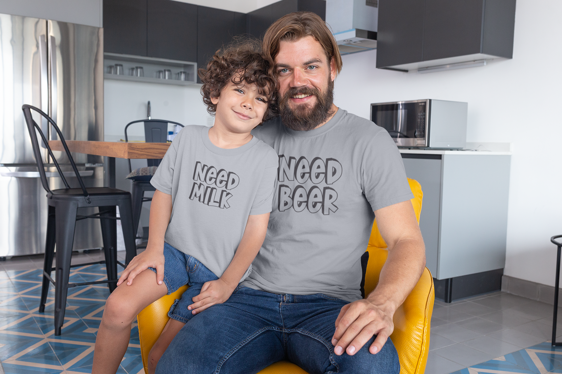 Dad and son wearing matching funny t-shirts at home that say “Need Beer” and “Need Milk”