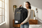 Woman holding a black garment bag with 'DR. AN' branding in a bedroom.