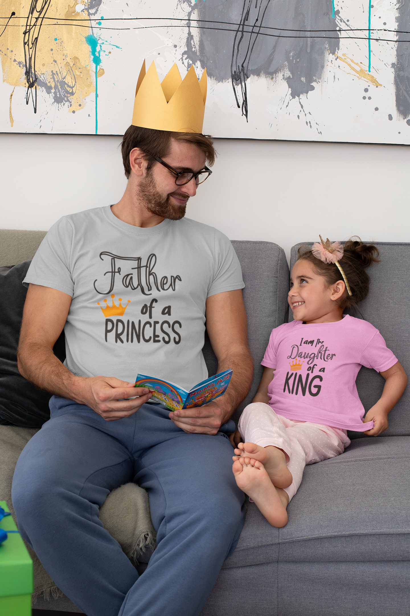 Dad reading to his daughter wearing matching Father’s Day t-shirts “Father of a Princess” and “Daughter of a King”