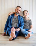 Father and son sitting at home wearing matching shirts that say “Mr. Fix It” and “Mr. Broke It”