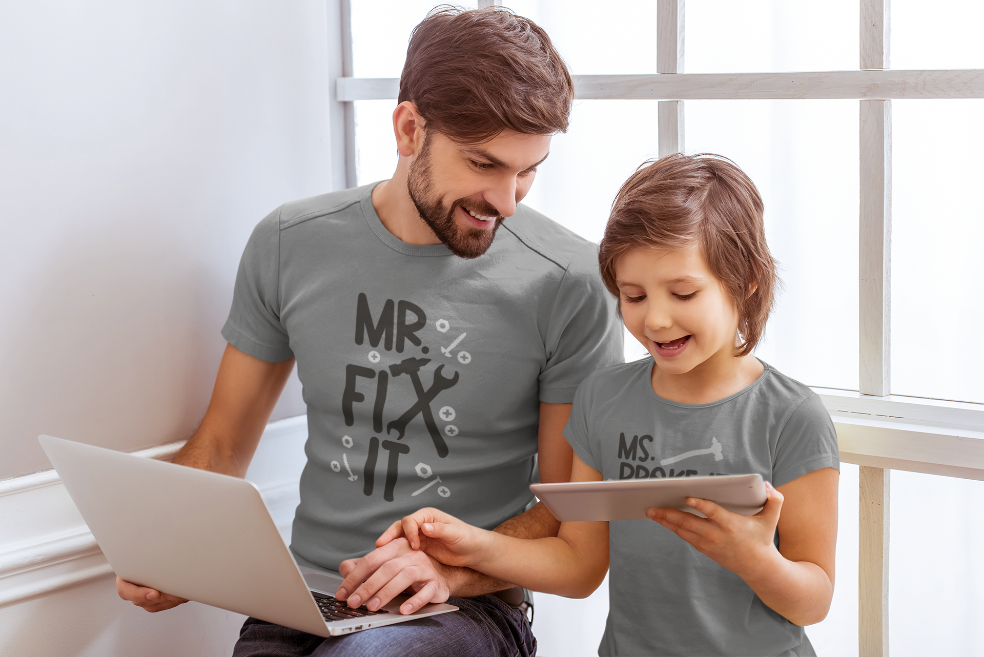 Dad and daughter using a laptop and tablet wearing matching shirts “Mr. Fix It” and “Ms. Broke It”