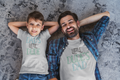 Dad and son lying on the floor wearing matching shirts “Little Dude’s Dad” and “Dad’s Little Dude”