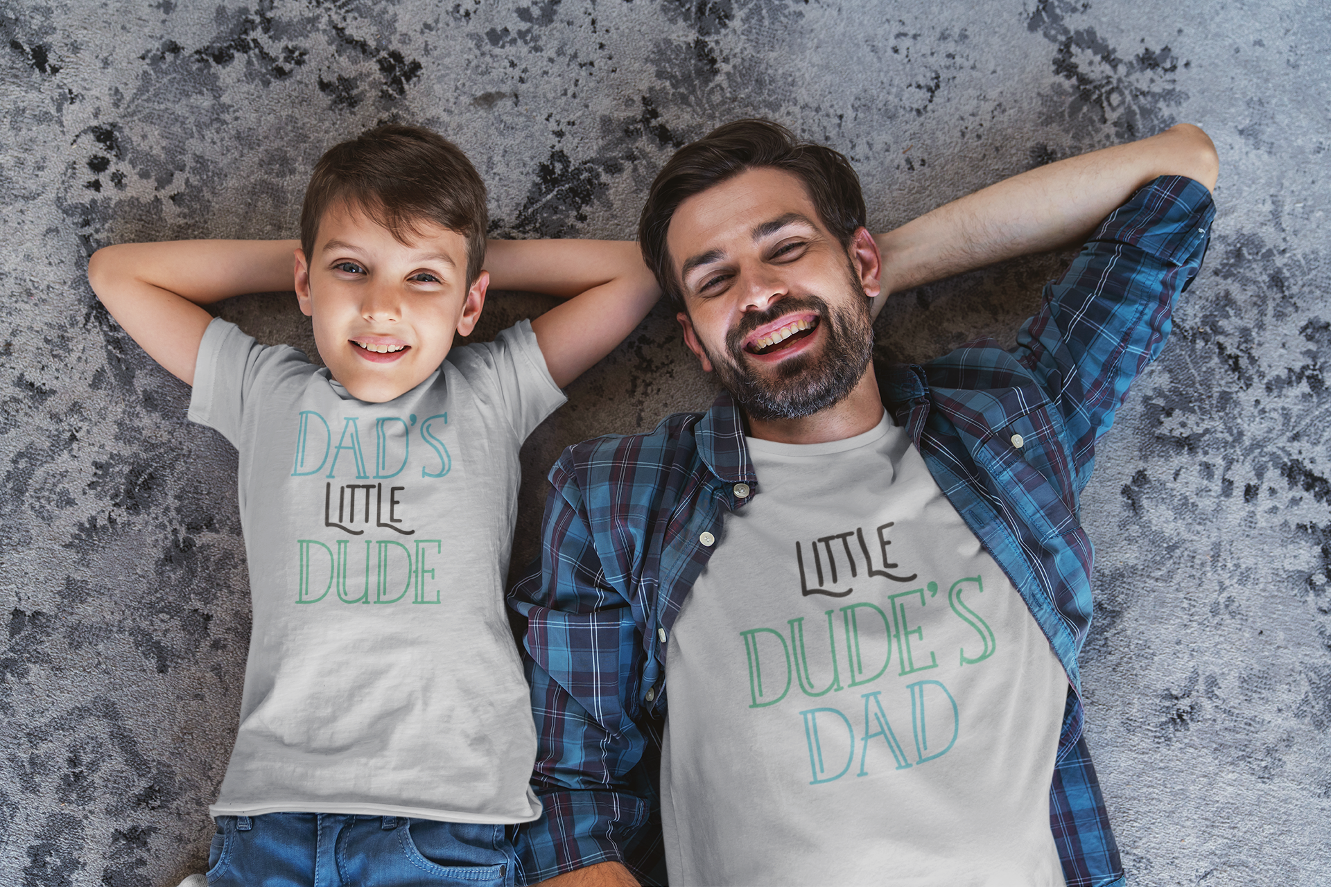Dad and son lying on the floor wearing matching shirts “Little Dude’s Dad” and “Dad’s Little Dude”