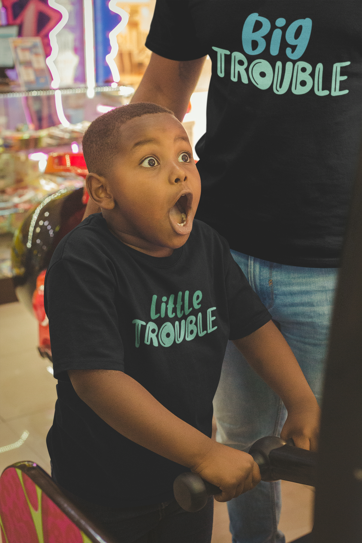 Dad and son at an arcade wearing matching shirts that say “Big Trouble” and “Little Trouble”