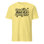 Yellow t-shirt with black text 'One cat short of a crazy lady' on a white background