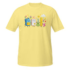 A light yellow short-sleeve crewneck t-shirt featuring a colorful cartoon graphic of school supplies (a blue backpack, notebook, scissors, ruler, and pencil) on the chest, displayed against a solid white background.