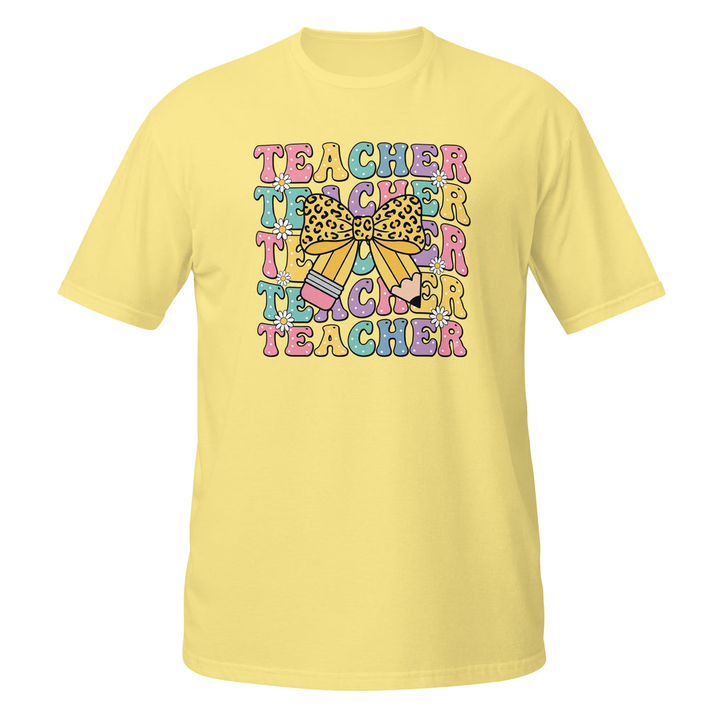 A pale yellow short-sleeve t-shirt with a colorful retro-style graphic on the chest that reads 'TEACHER TEACHER TEACHER' in pastel letters, decorated with a bow and pencil illustration.